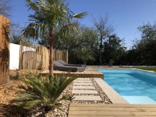 Jardin bord de mer en bordure de piscine avec terrasse bois, ganivelles, graviers, palmiers, travertin à La Chapelle Hermier (85)