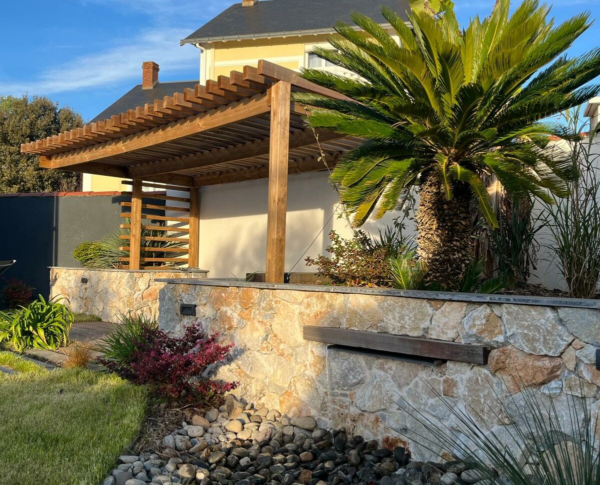 Aménagement d'un petit jardin avec mur en pierres, lame d'eau incrustée, pergola en bois exotique et végétaux aux Sables D'Olonne (85)