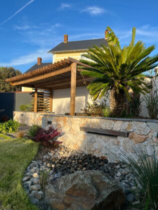 Aménagement d'un petit jardin avec mur en pierres, lame d'eau incrustée, pergola en bois exotique et végétaux aux Sables D'Olonne (85)